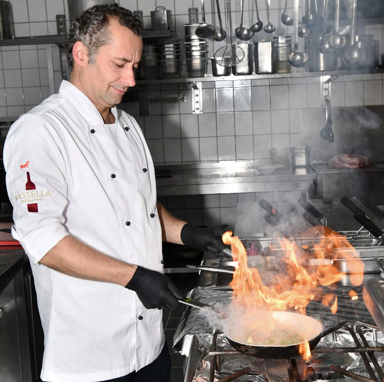 Ein Koch des Ristorante Pasta & Vino flambiert ein Gericht in einer Pfanne in einer Küche.