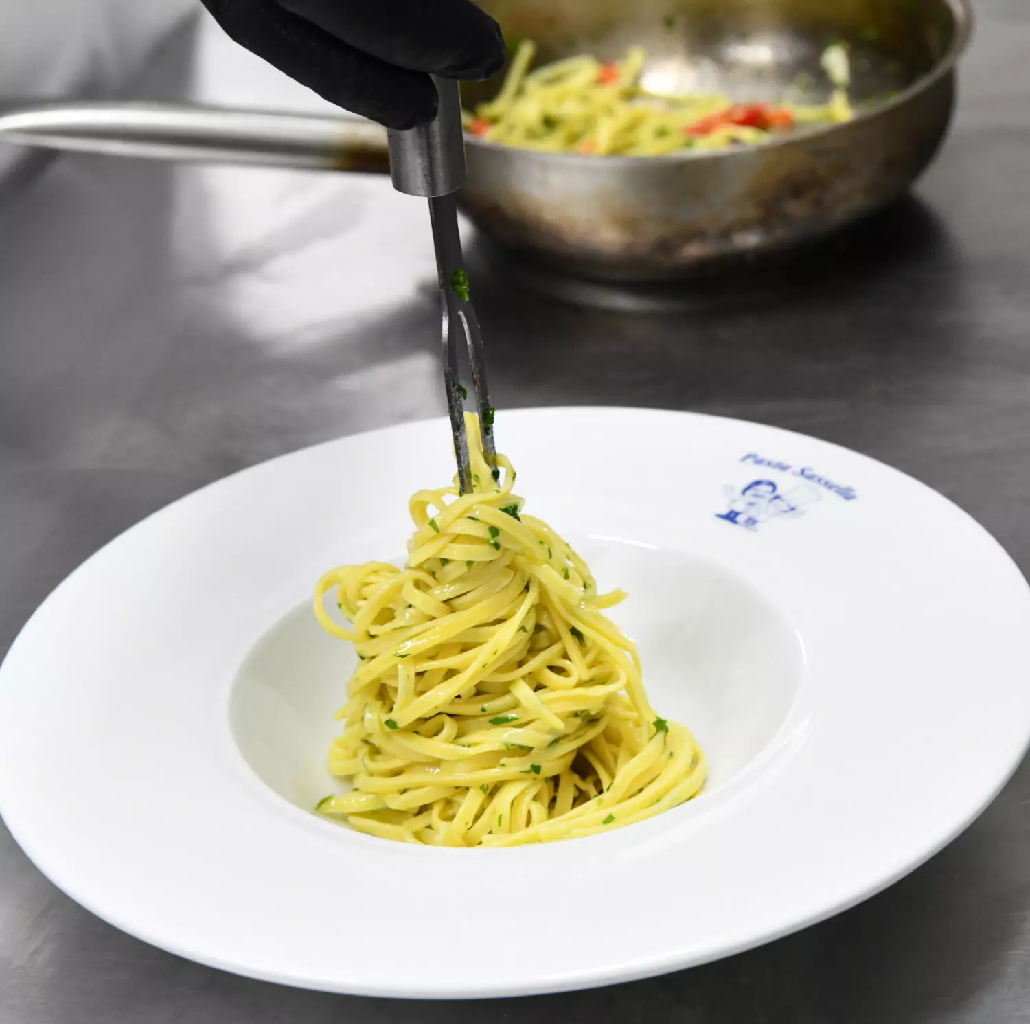 Koch des Ristorante Pasta & Vino richtet Spaghetti mit Kräutern auf einem weißen Teller an.